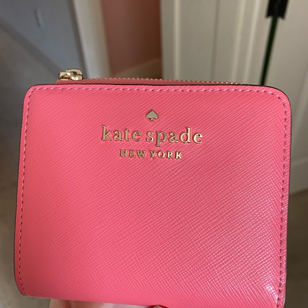 This is a Kate Spade coral, pink blindfold compact wallet.